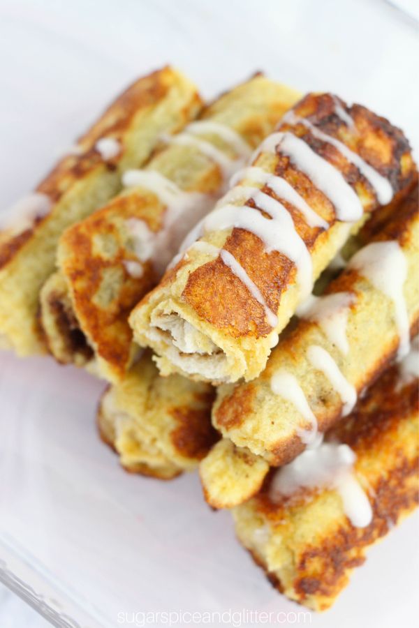 overhead image of a stack of cinnamon bun french toast roll-ups drizzled with cream cheese frosting