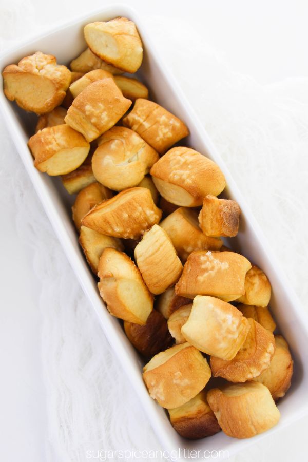 overhead image of a white dish full of golden, soft pretzel bites with a cheese dipping sauce in the background