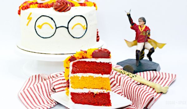 close-up image of a slice of Harry Potter cake with layers of maroon and gold cake with a Harry Potter figurine and the full cake in the background