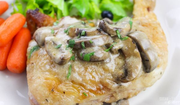 close-up image of browned chicken quarters smothered with creamy mushroom sauce on a white plate