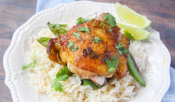 a golden lime cilantro chicken thigh on a bed of rice on a whilte plate