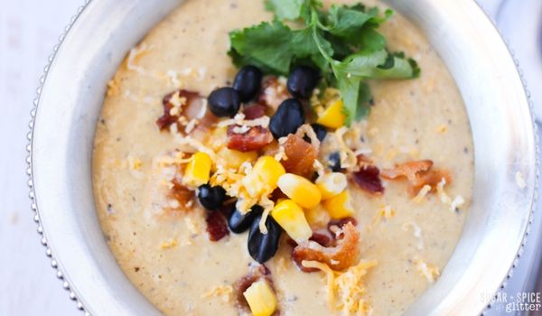 overhead image of corn chowder in a silver bowl with corn, black beans, bacon, cilantro and cheese sprinkled on top