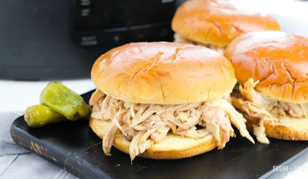 sandwiches filled with mississippi chicken on a black tray in front of a crockpot