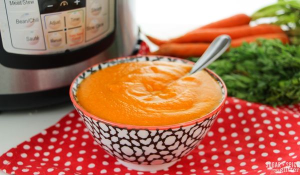 close-up image of a black and white bowl filled with carrot ginger soup with carrots and an Instant Pot in the background