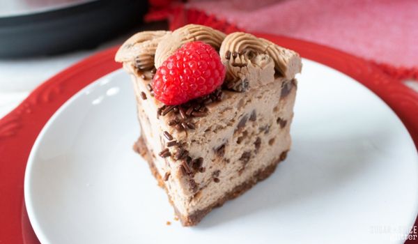 a slice of chocolate cheesecake with chocolaet sprinkles and a raspberry on top