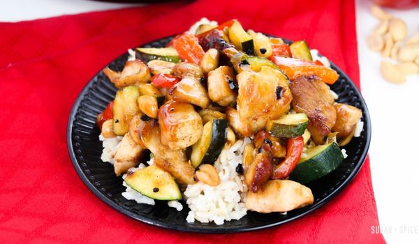Kung Pao chicken on a bed of rice on a black circular plate set on a red napkin