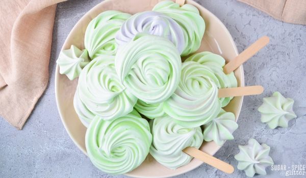 overhead image of green and lavendar-swirled meringue cookie pops in a beige bowl