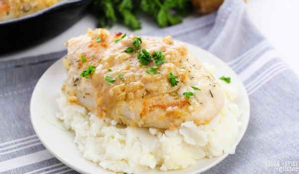 chicken breast smothered in onion gravy and garnished with parsley overtop of a bed of mashed potatoes on a white plate on a gray napkin