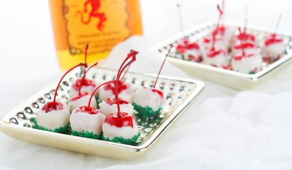white chocolate-coated cherries with Christmas sprinkles on a gold plate with a bottle of cinnamon whiskey in the background