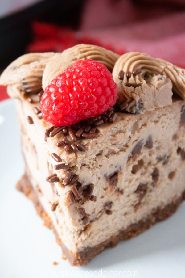 close-up picture of a slice of chocolate cheesecake with chocolaet sprinkles and a raspberry on top