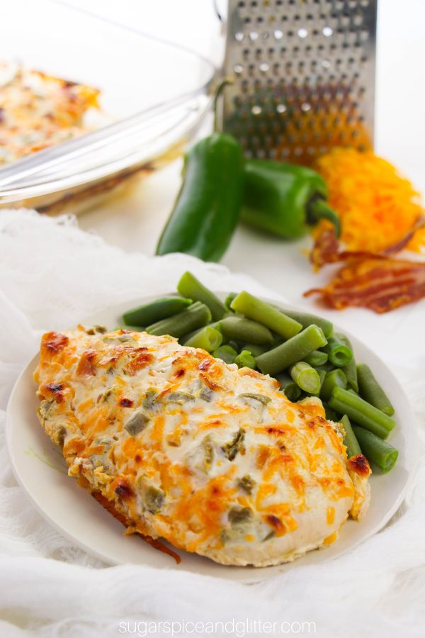 a whole jalapeño popper chicken on a white plate with a side of green beans, with ingredients needed to make the recipe in the background