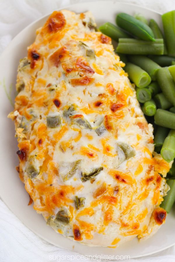 close-up image of a whole jalapeño popper chicken on a white plate with a side of green beans
