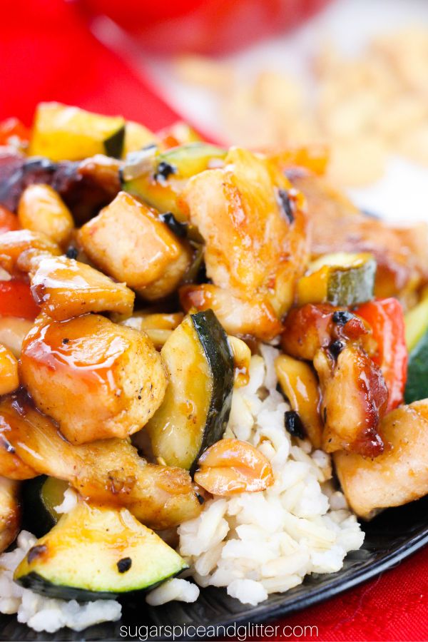 Kung Pao chicken on a bed of rice on a black circular plate set on a red napkin