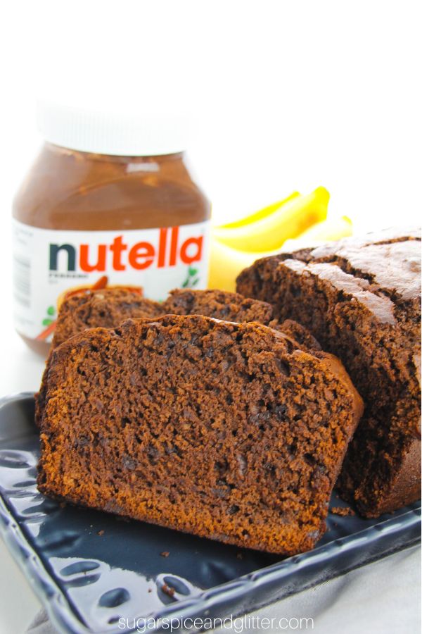 two slices of Nutella Banana Bread on a navy platter, with ingredients needed to make the recipe in the background