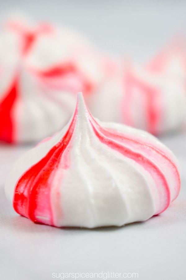a close-up image of a piped red and white peppermint meringue cookie on a white background