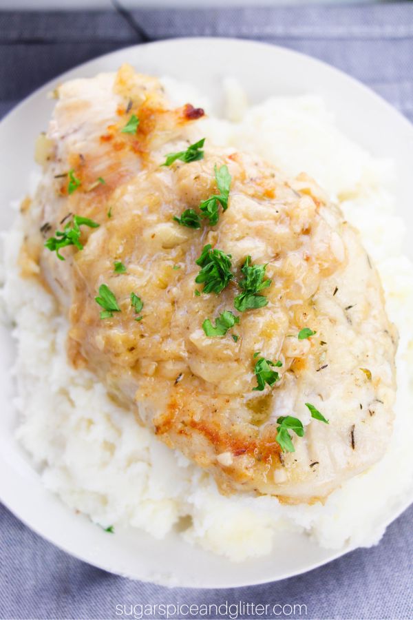 close-up image of a chicken breast smothered in onion gravy and garnished with parsley overtop of a bed of mashed potatoes on a white plate