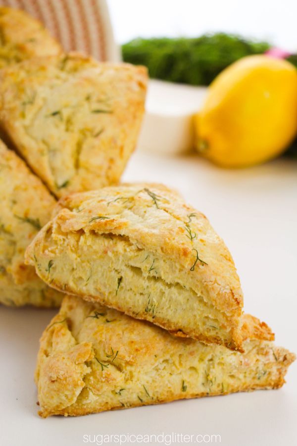 lemon dill scones tumbling out of a white fabric basket with lemon, dill and feta in the background