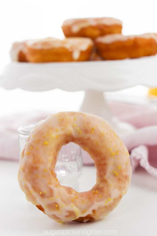 a lemon-glazed donut stood on it's end in front of a white pedestal holding more donuts