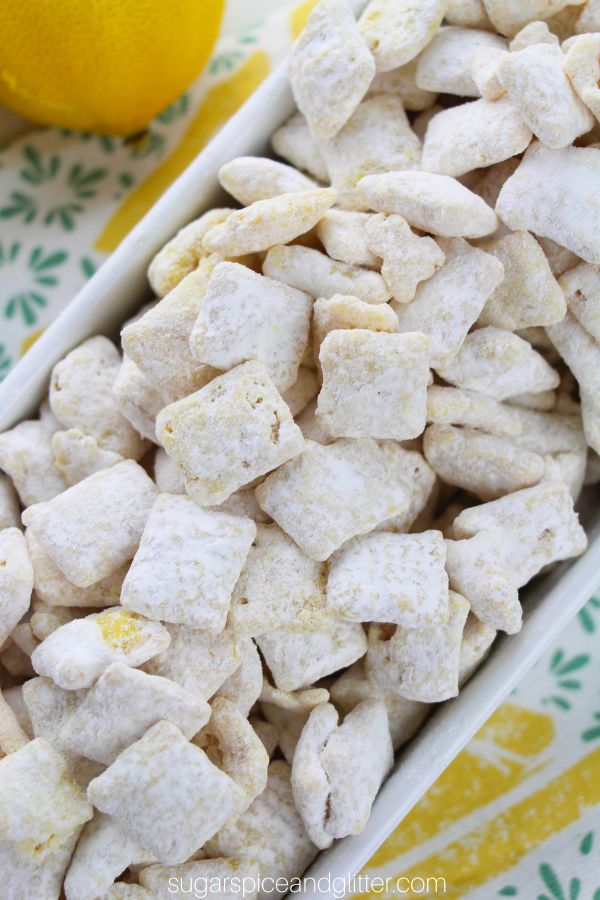overhead picture of a white bowl filled with lemon muddy buddies on top of a lemon-print napkin