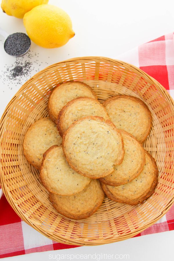 overhead image of lemon poppyseed cookies set on a wicker tray on a red plaid napkin with lemons and poppyseeds in the background