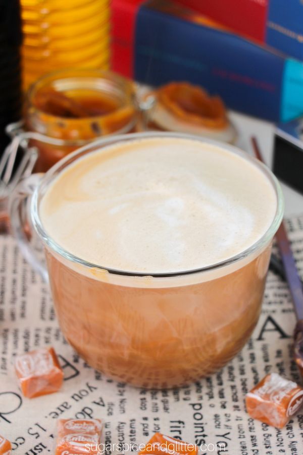 glass mug filled with butterbeer latte on a newsprint napkin with caramel squares and wands scattered around it