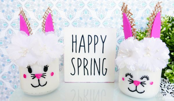 two painted bunny mason jars displayed on a mint-colored pedestal with a "Happy Spring" wooden sign
