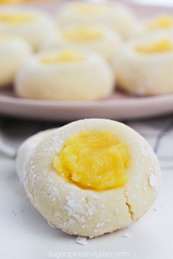 a close-up image of a lemon thumbprint cookie in front of a pink plate holding more cookies
