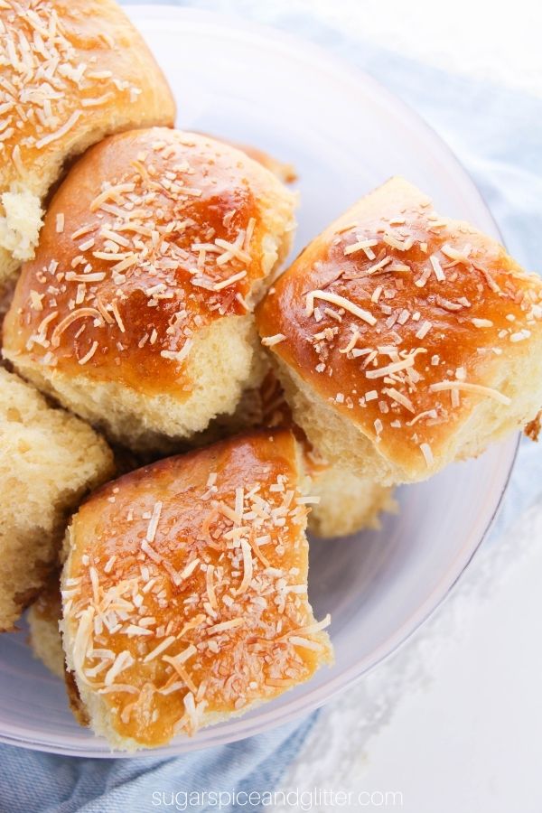 golden Hawaiian dinner rolls garnished with toasted coconut in a pink bowl set on a denim napkin
