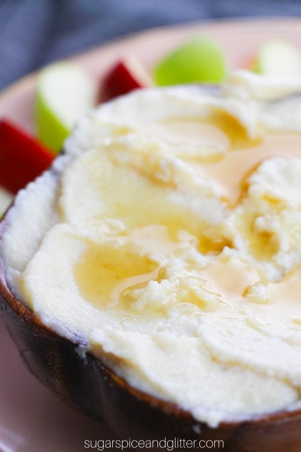 close-up image of honeyed ricotta in a wooden bowl with apple slices in the background