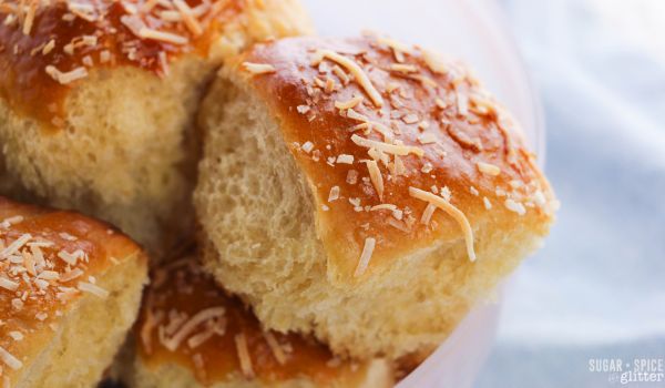 golden Hawaiian dinner rolls garnished with toasted coconut in a pink bowl set on a denim napkin