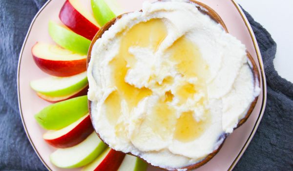 overhead image of honeyed ricotta in a wooden bowl along with red and green apple slices on a pink plate