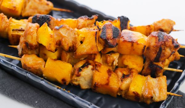 a pile of chipotle chicken and mango skewers set on a navy blue platter
