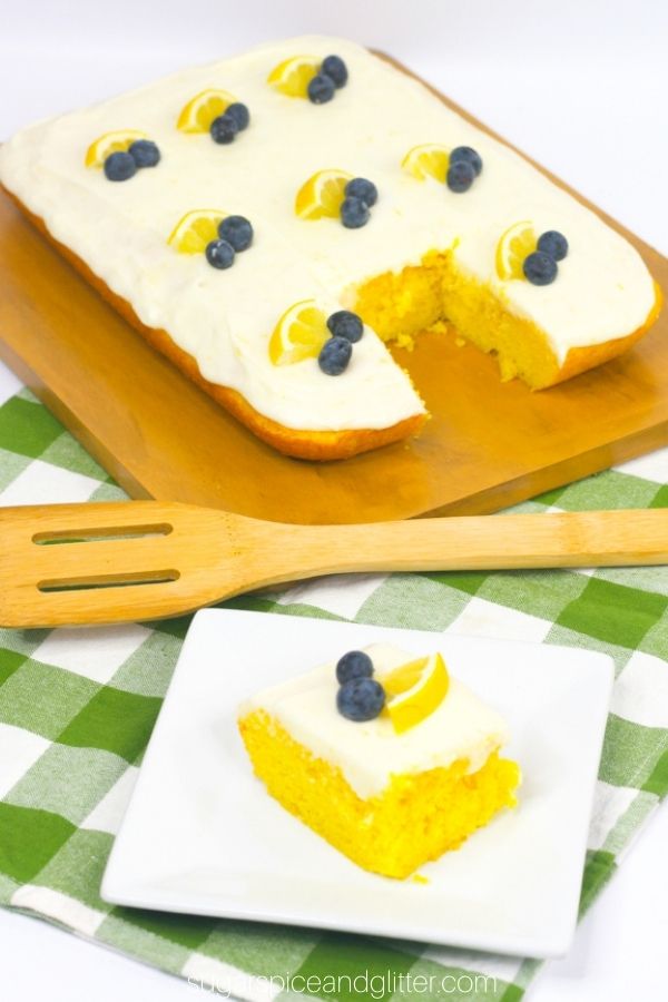 a square of lemon sheet cake on a white plate, set in front of the whole cake on a green plaid napkin