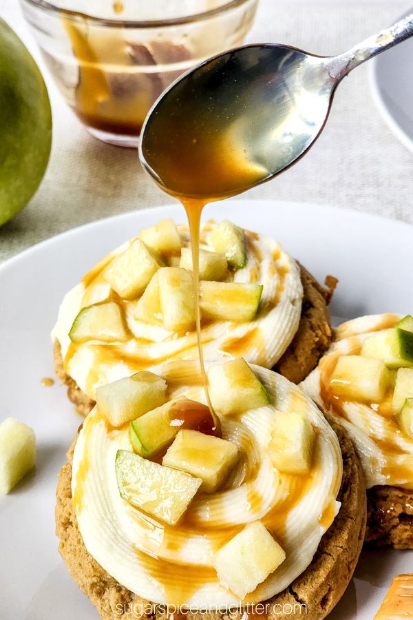 close up image of drizzling caramel overtop of caramel apple cookies, brown cookies with cream cheese frosting swirled on and Granny Smith apple pieces sprinkled onto the frosting
