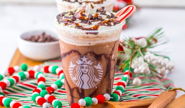 a clear Starbucks cup holding a peppermint mocha frappuccino topped with whipped cream, chocolate and a candy cane