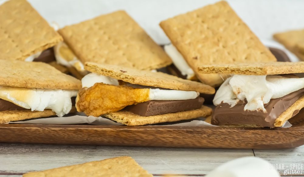 a wooden platter with several toasted s'mores set on top